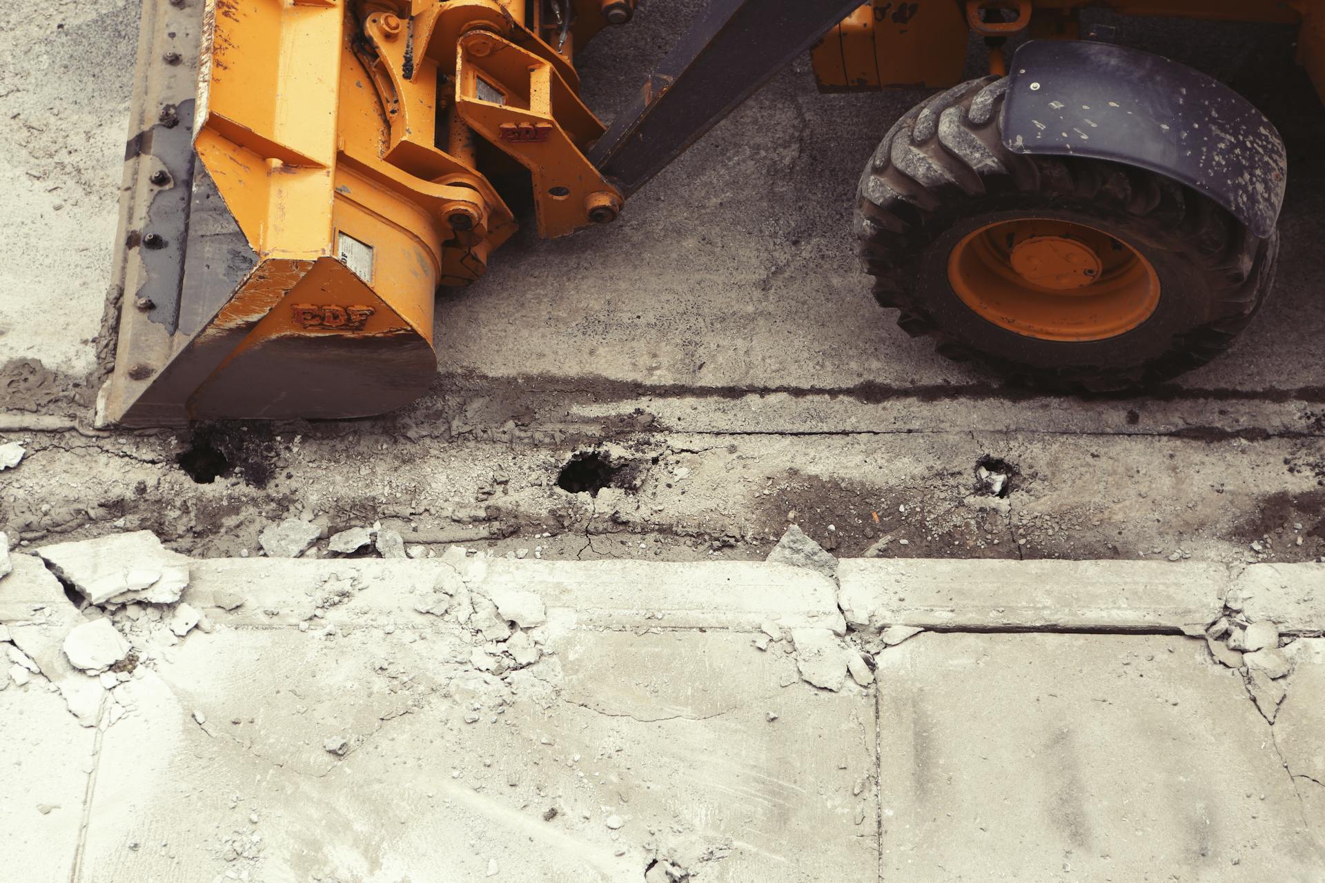 Construction truck next to a broken sidewalk.