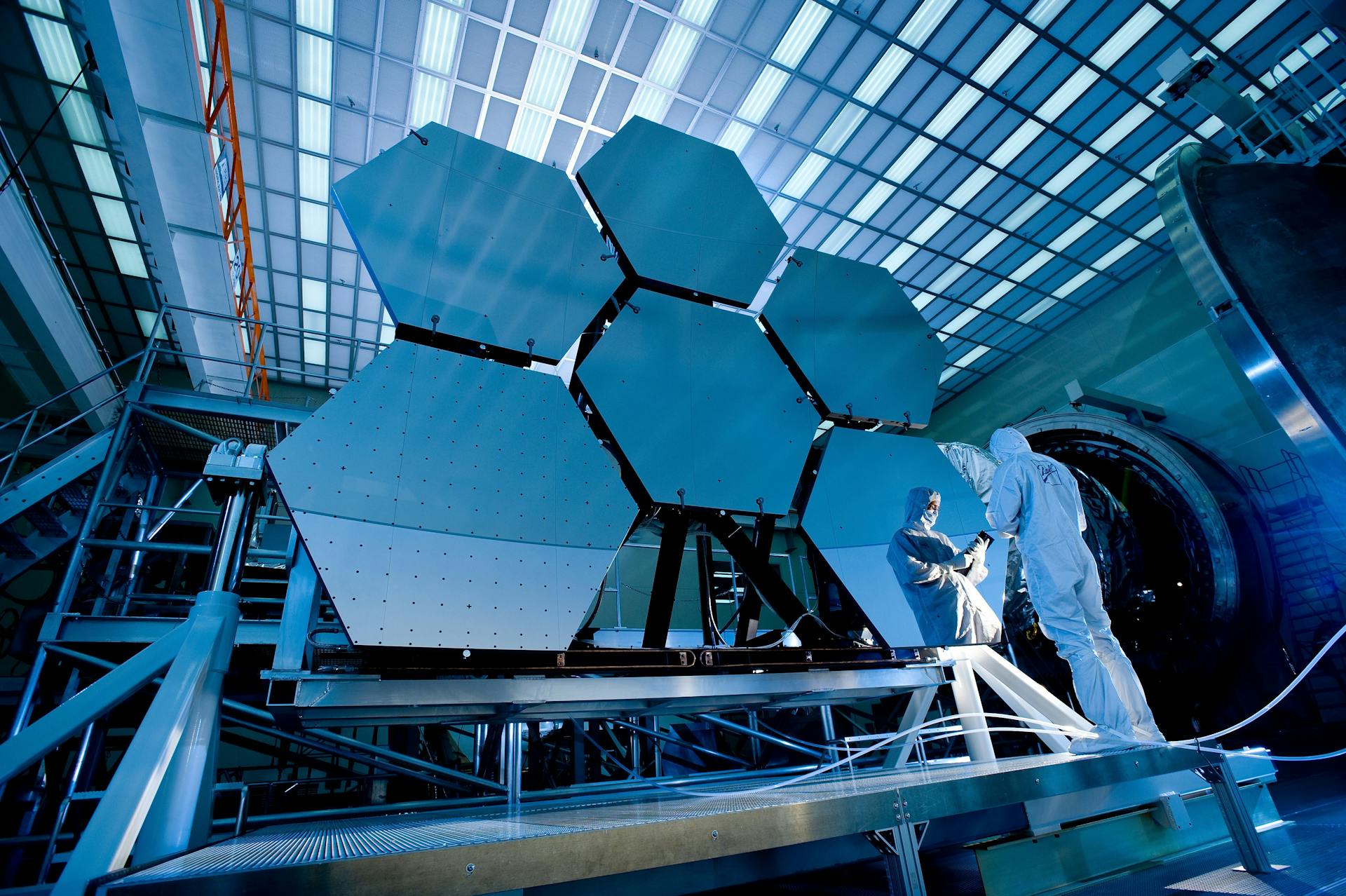 Two people are working on the mirrors of a telescope.