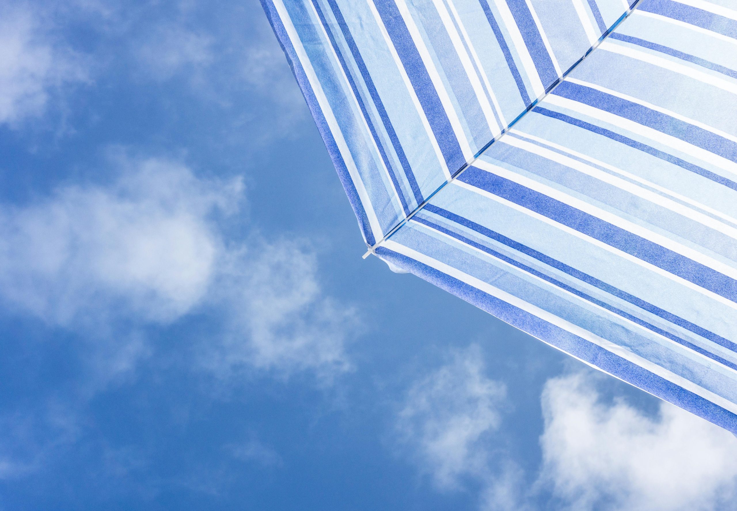Blue and white parasol with a view of a sunny blue sky dotted with a few clouds